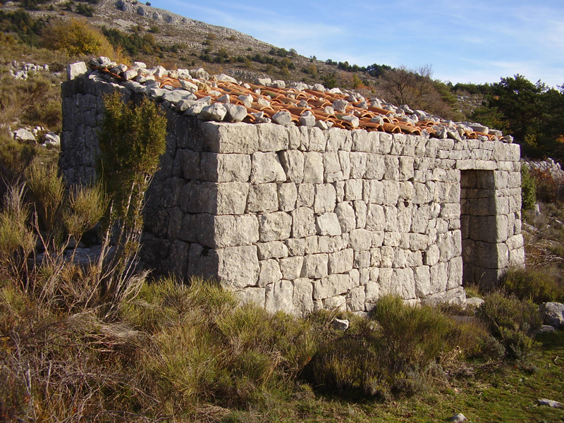 Lieu-dit Le Ferrier  Saint-Vallier-de-Thiey (Alpes-Maritimes) : cabanon de plan rectangulaire,  faade en gouttereau et  toit  une pente couvert de tuiles canal lestes de petites pierres. Photo de Jean Laffitte.